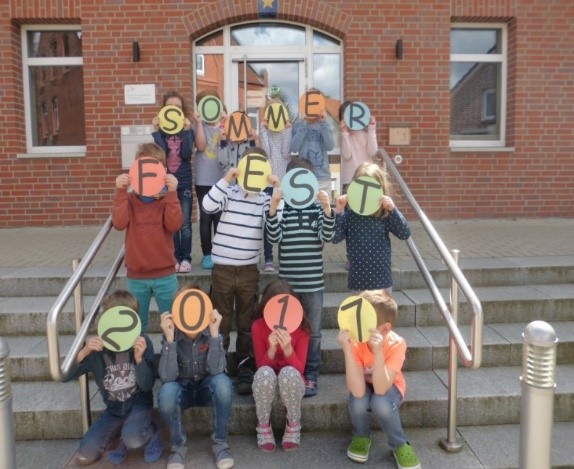 Gruppe von Kindern vor dem Familienzentrum halten Schilder mit dem Schriftzug Sommerfest 2017 hoch