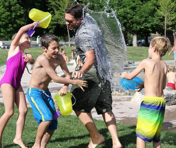 Drei Kinder bewerfen einen Mann mit Wasser. Alle lachen.