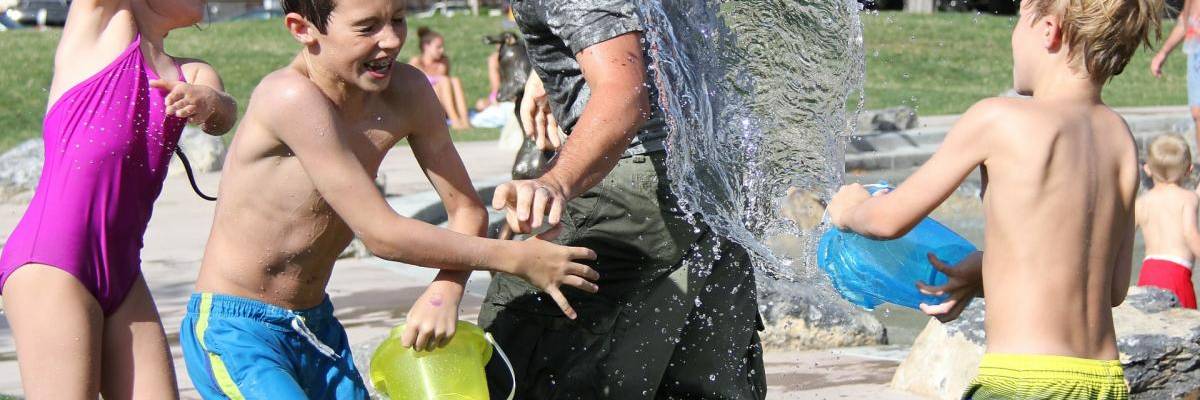 Drei Kinder bewerfen einen Mann mit Wasser. Alle lachen.