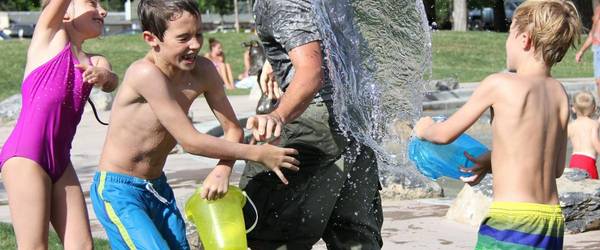 Drei Kinder bewerfen einen Mann mit Wasser. Alle lachen.