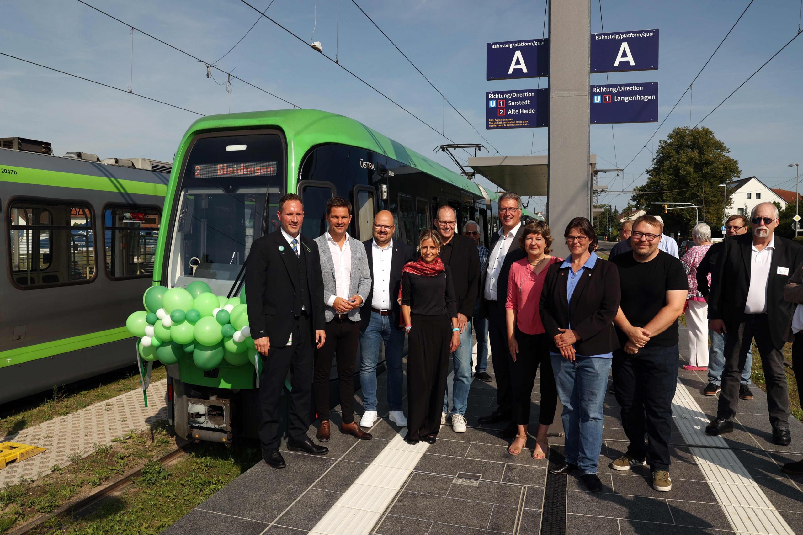 Eine Gruppe Menschen steht vor einer mit grünen Luftballons geschmückten Stadtbahn.