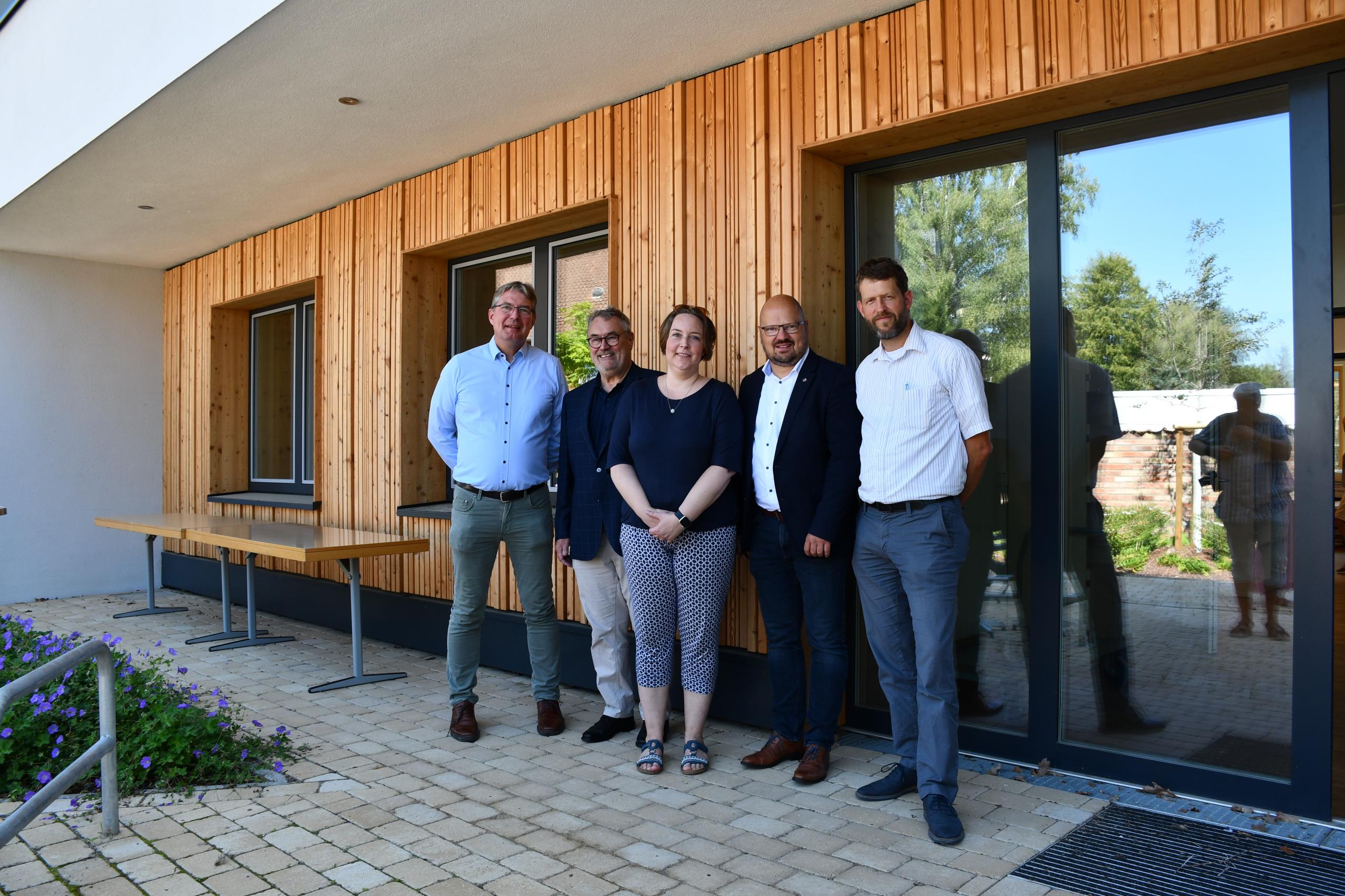 Fünf Menschen stehen vor einem Gebäude mit einer neuen Holzfassade.