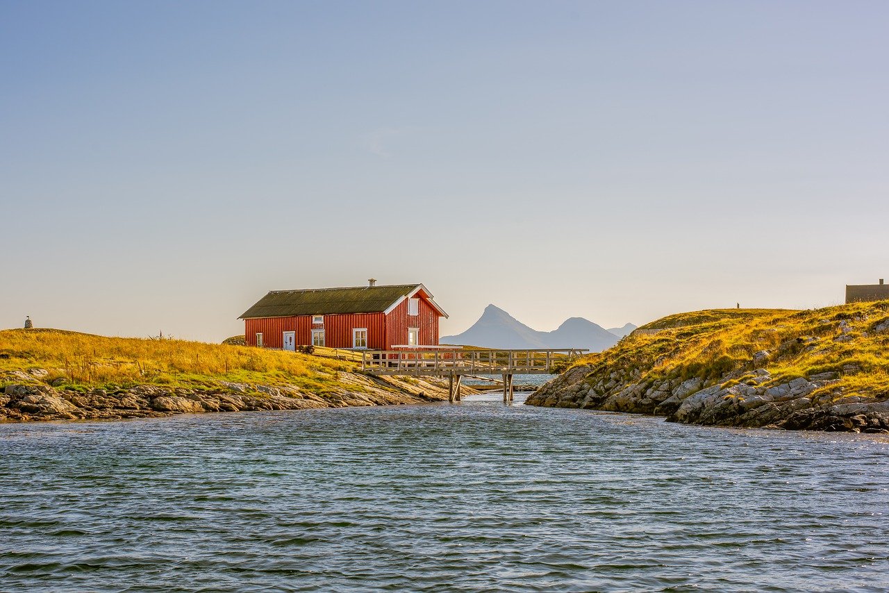 Haus am Fjord auf einem grün bewachsenen Hügel mit einer Holzbrücke davor