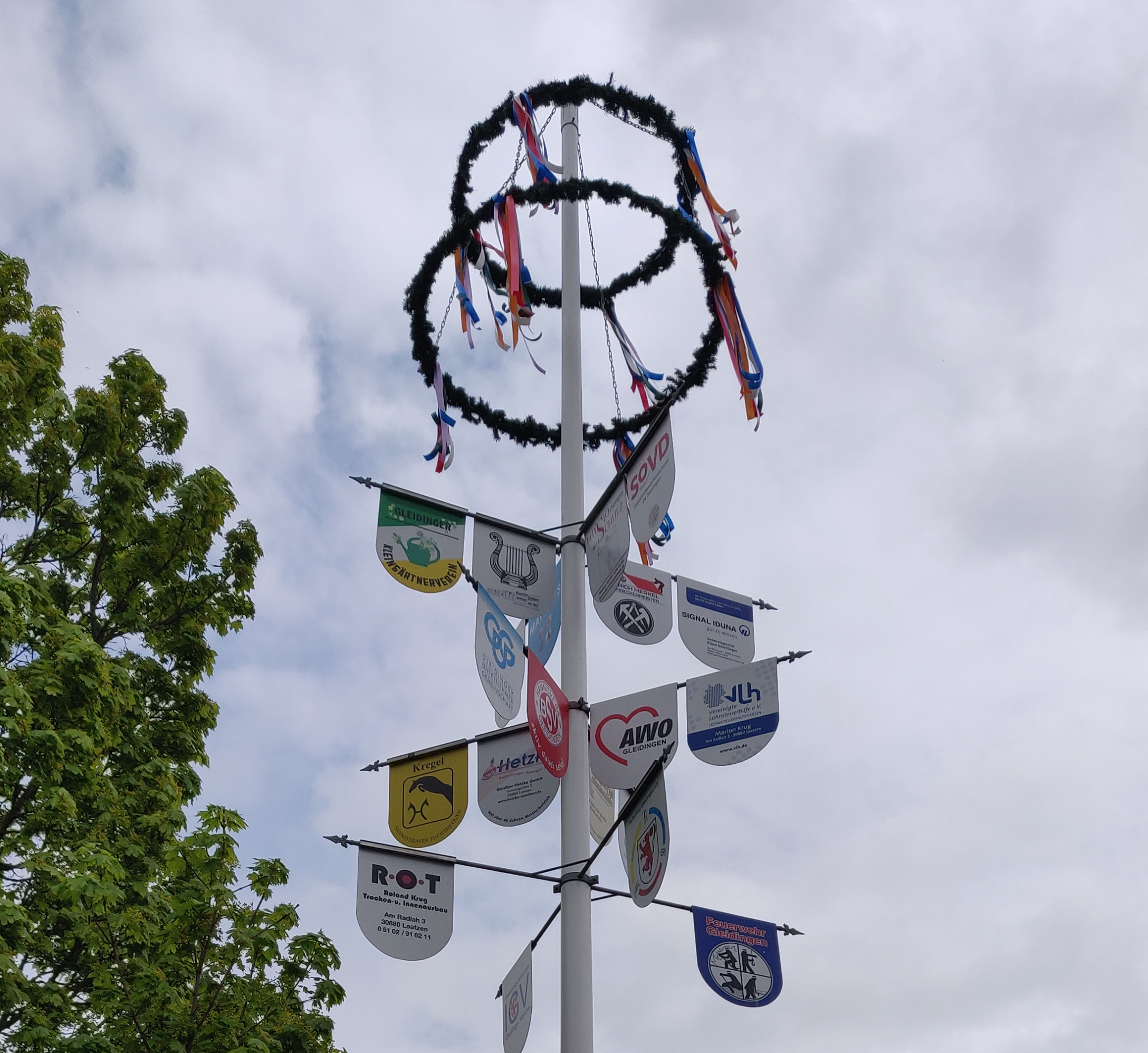 Maibaum mit Schildern verschiedener Unternehmen und Maikranz