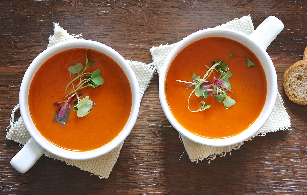 Zwei weiße Tassen mit Tomatensuppe gefüllt.