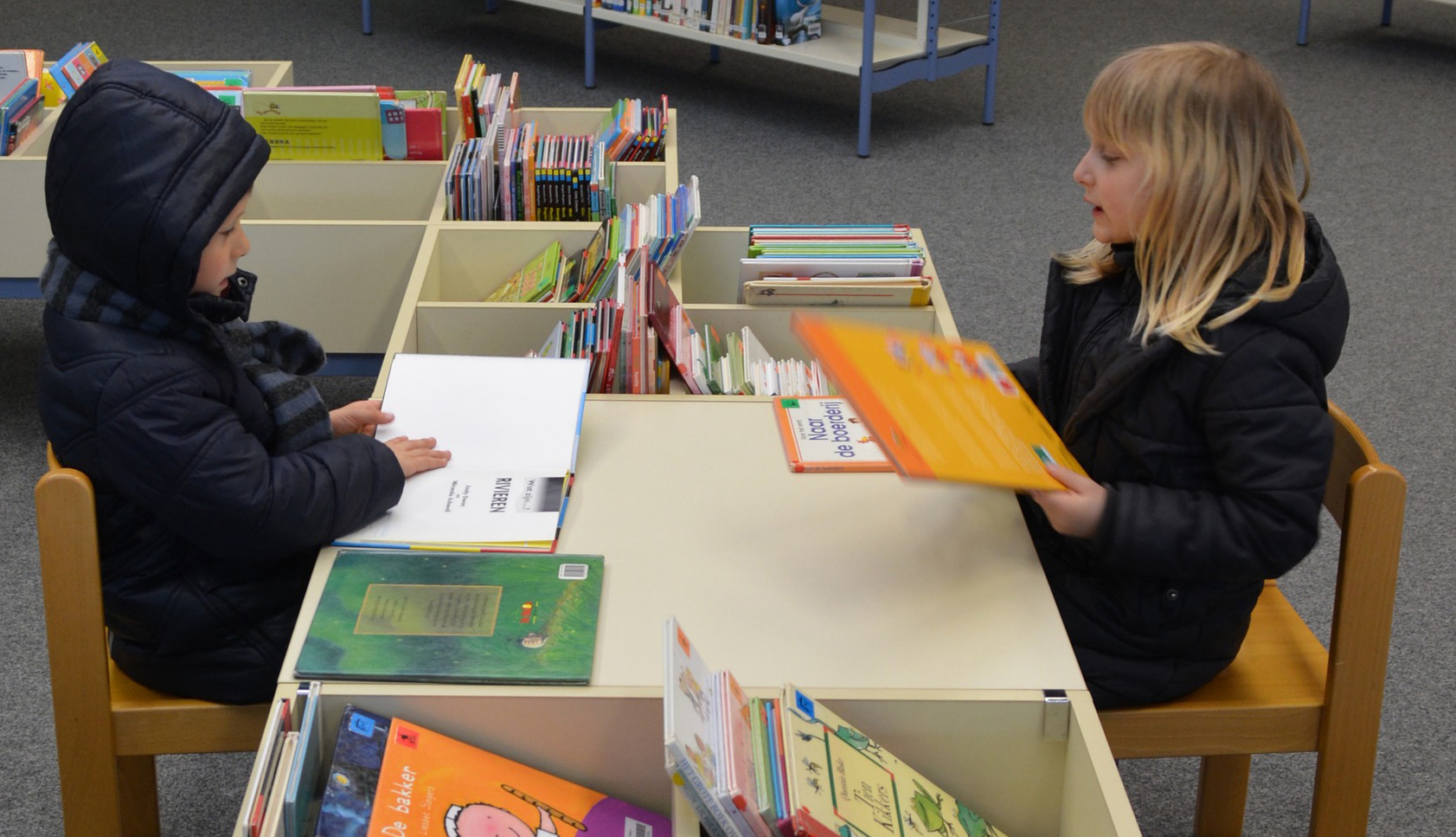 Zwei Kinder sitzen sich gegenüber und schauen sich Bücher an