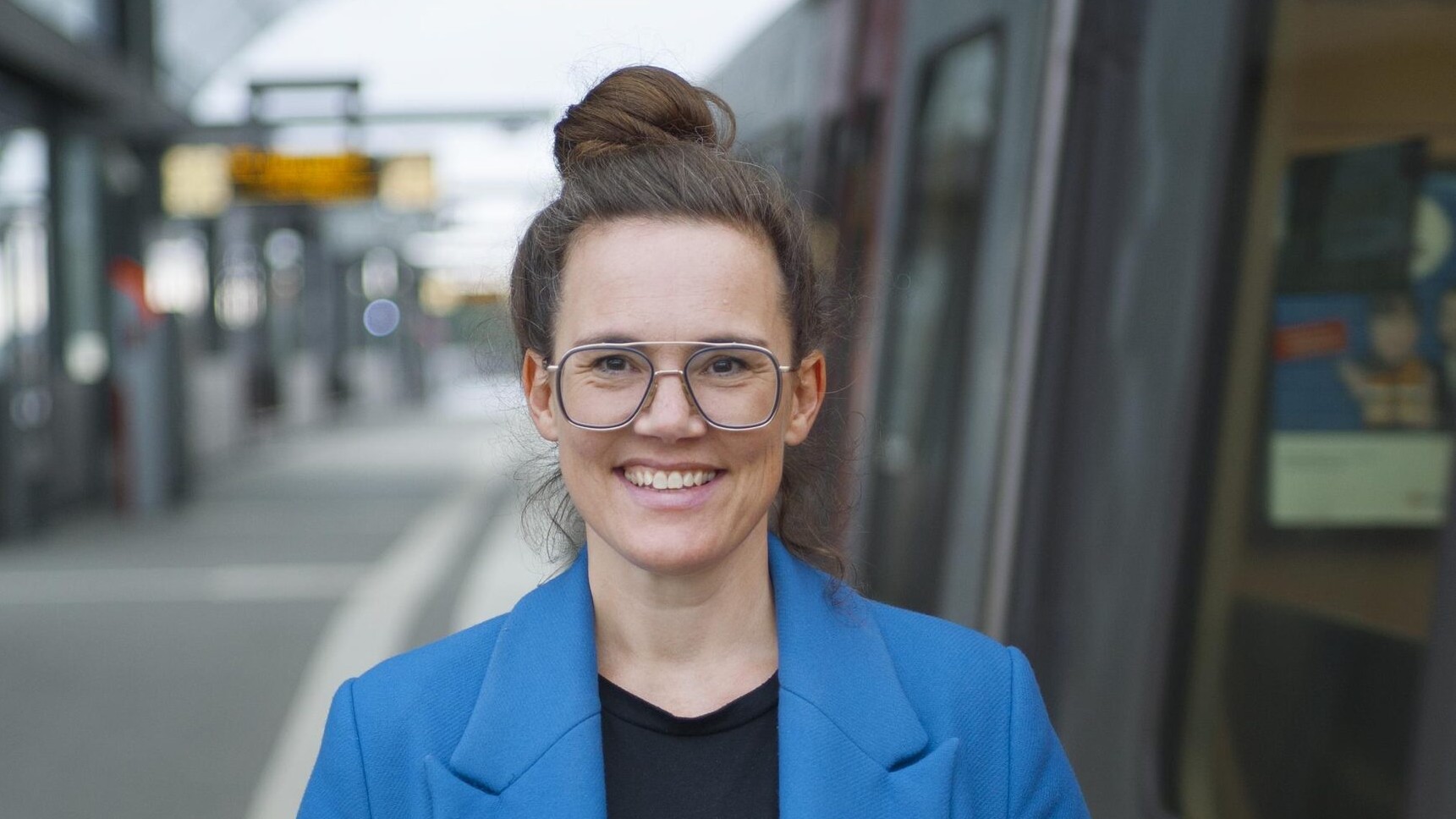 Eine Frau in blauem Mantel steht an einem S-Bahnhof. Ein Zug ist eingefahren.