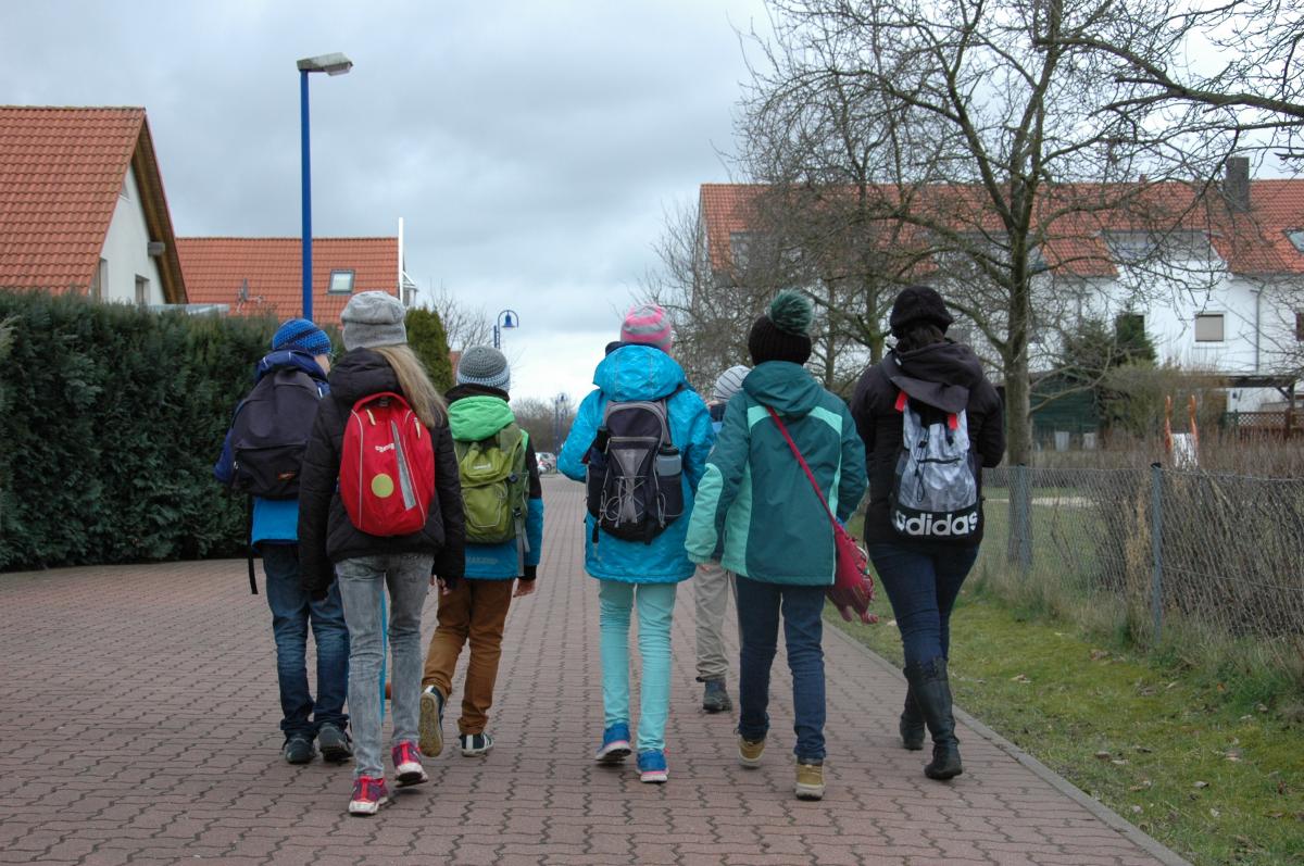 Eine Gruppe von Kindern gehen einen gepflasterten Weg entlang. Die Gruppe ist von hinten zu sehen.