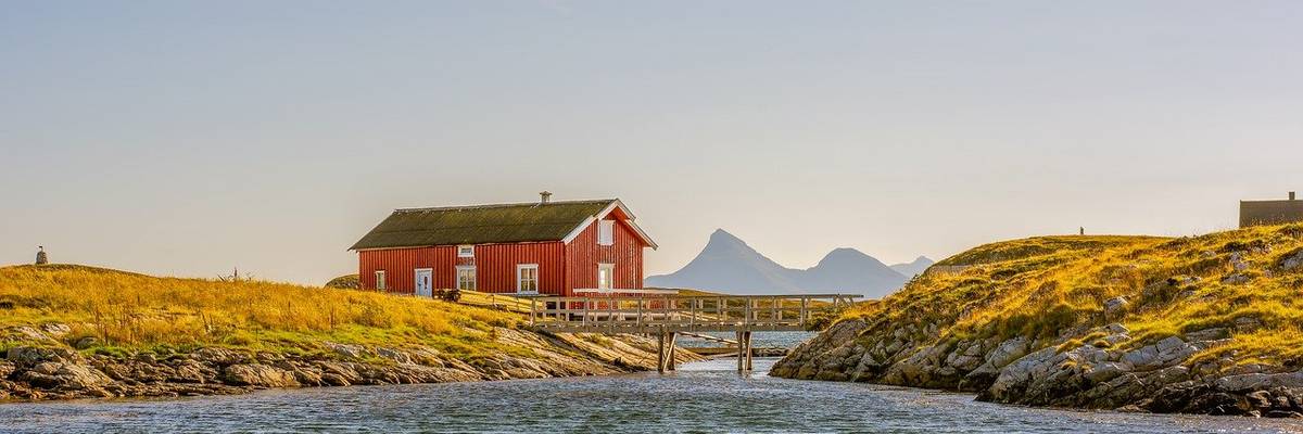 Haus am Fjord auf einem grün bewachsenen Hügel mit einer Holzbrücke davor