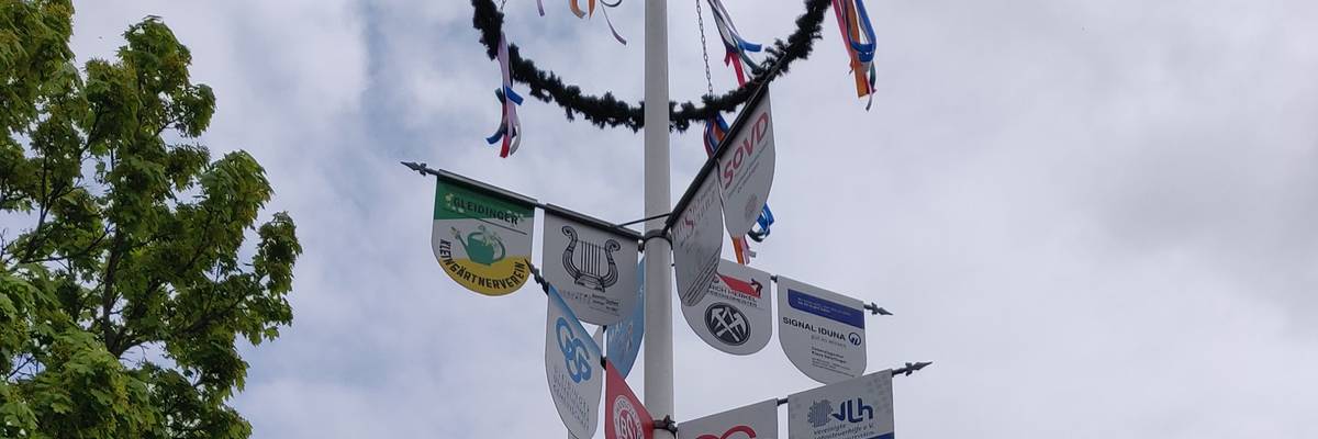 Maibaum mit Schildern verschiedener Unternehmen und Maikranz