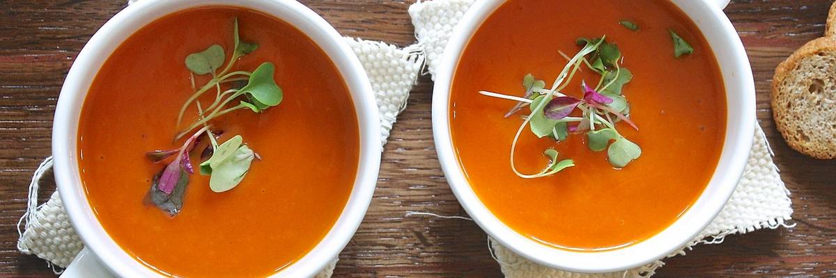 Zwei weiße Tassen mit Tomatensuppe gefüllt.