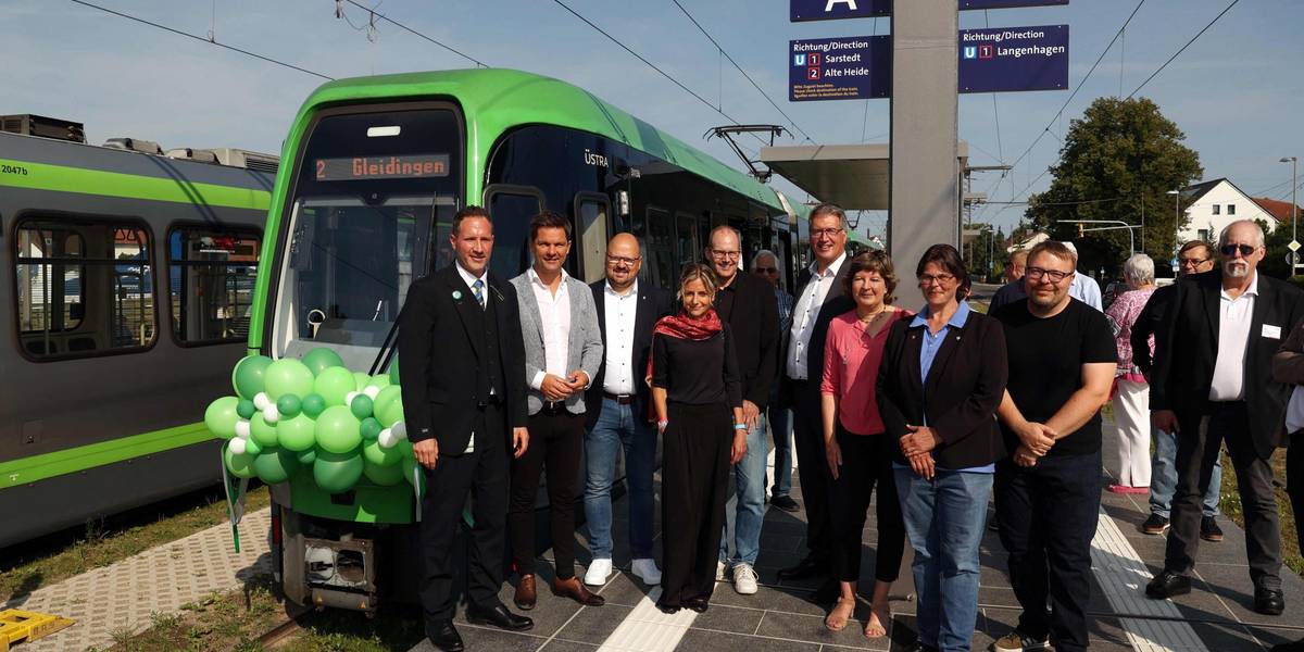 Eine Gruppe Menschen steht vor einer mit grünen Luftballons geschmückten Stadtbahn.