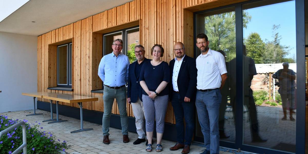 Fünf Menschen stehen vor einem Gebäude mit einer neuen Holzfassade.