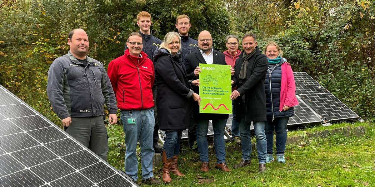 Eine Gruppe Frauen und Männer stehen vor Solarmodulen in einem herbstlichen Garten.