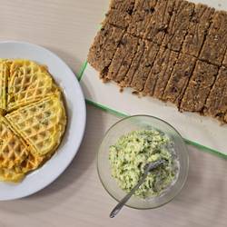 Es steht ein Teller mit Waffeln auf dem Tisch. Ein Teller mit einem Dip. Ein Teller mit Müsliriegeln. Das haben alle Küchenkräfte hergestellt.