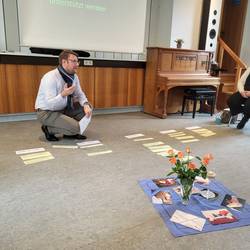 Pastor Dr. Jens Wening kniet auf dem Boden und ordnet mit Karten die Entwicklung des Todesverständnisses dem Alter der Kinder zu.