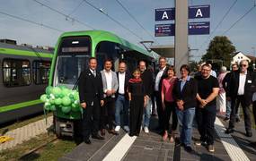 Eine Gruppe Menschen steht vor einer mit grünen Luftballons geschmückten Stadtbahn.