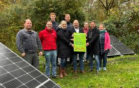 Eine Gruppe Frauen und Männer stehen vor Solarmodulen in einem herbstlichen Garten.