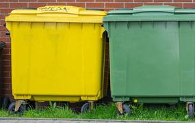 EIn gelber Container steht vor einer geklinkerten Fassade auf dem Rasen.