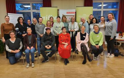 Eine Gruppe Frauen sitzen als Gruppe vor Stellwänden.