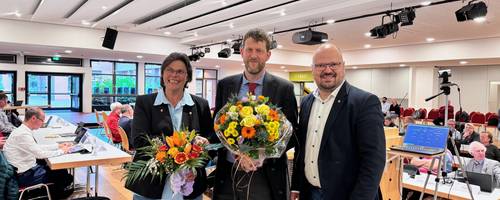 Der neue Stadtrat Hauke Schröder steht mit einem Blumenstrauß neben Kai Eggert und Silke Rehmert.