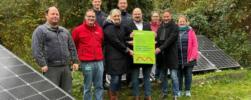 Eine Gruppe Frauen und Männer stehen vor Solarmodulen in einem herbstlichen Garten.