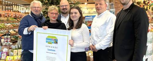 Eine Gruppe Personen steht vor einem Tannenbaum und einem Tisch mit Lebensmitteln