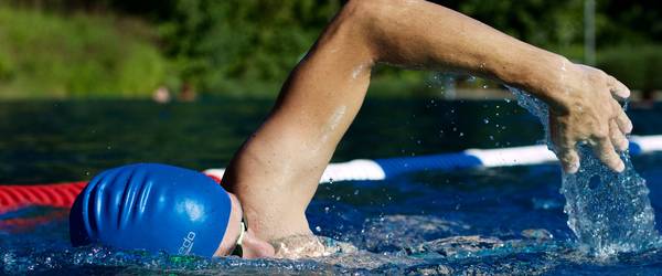 Ein kraulender Schwimmer mit blauer Badekappe zieht in einem See seine Bahnen