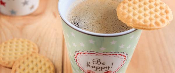 Kaffeebecher mit dem Aufdruck "be happy" und Keksen