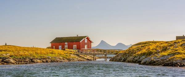 Haus am Fjord auf einem grün bewachsenen Hügel mit einer Holzbrücke davor