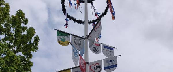 Maibaum mit Schildern verschiedener Unternehmen und Maikranz