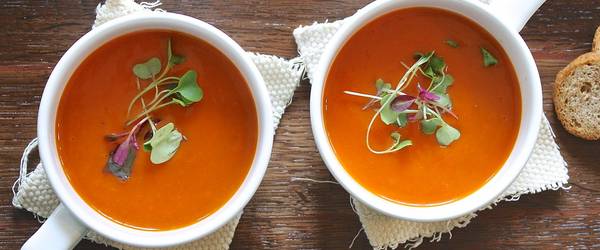 Zwei weiße Tassen mit Tomatensuppe gefüllt.